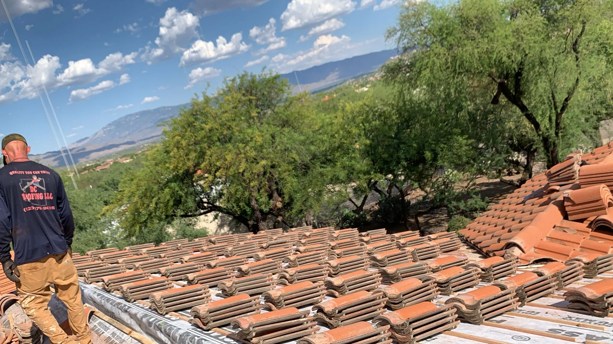 DC Roofing crew member on a tile roof in Tucson, AZ with Santa Catalina Mountains in the background
