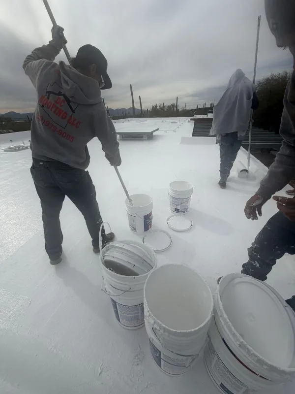 DC Roofing crew applying white reflective coating to a flat roof in Tucson
