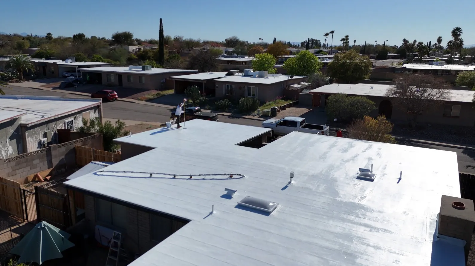 DC Roofing worker applying white elastomeric coating on a flat roof in a Green Valley neighborhood