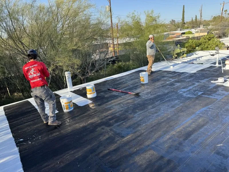 Two workers rolling white reflective roof coating onto a flat roof